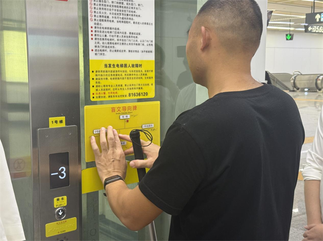 图为商磊正在触摸长沙地铁站的盲文导向牌